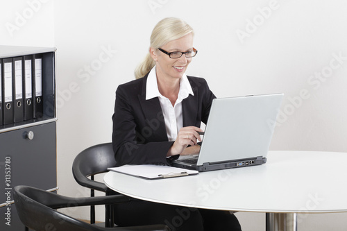 Frau am Schreibtisch lachend mit Laptop und Brille