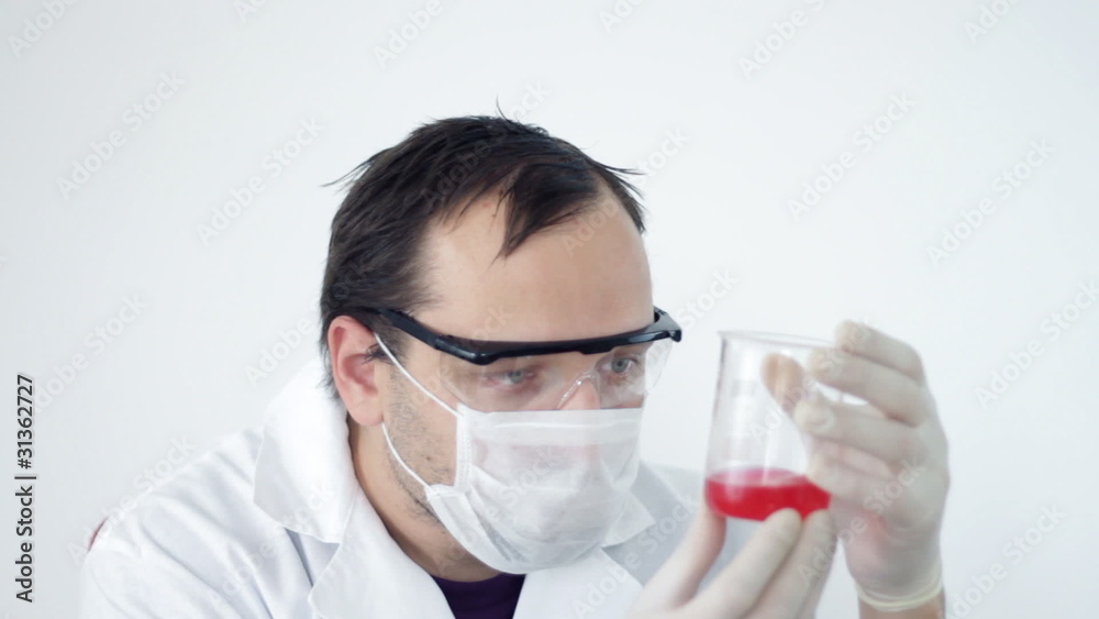 Male scientist examining beaker with red liquid Male scientist examining beaker with red liquid