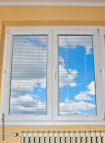 Blue sky with thick white clouds behind closed window.