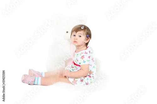 little girl sits on a white sheep skin with the big toy bear