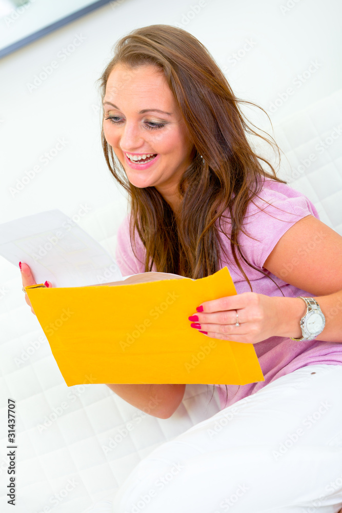 Pleased pretty woman sitting on sofa and reading letter. Pleased pretty woman sitting on sofa and reading letter.