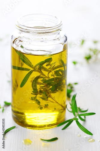 Scented oil with rosemary and fresh herbs on white wooden backgr