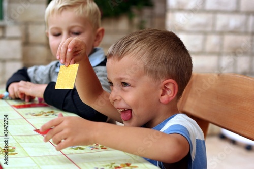 Two boys play a board game, one boy shows a card and