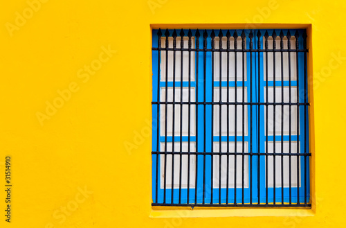 Blue window on a bright yellow wall © kmiragaya