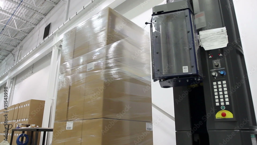 A shrink wrap machine covers a large stack of boxes

