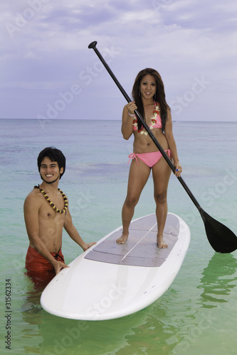 hawaiian beachboy teaches young woman to paddleboard