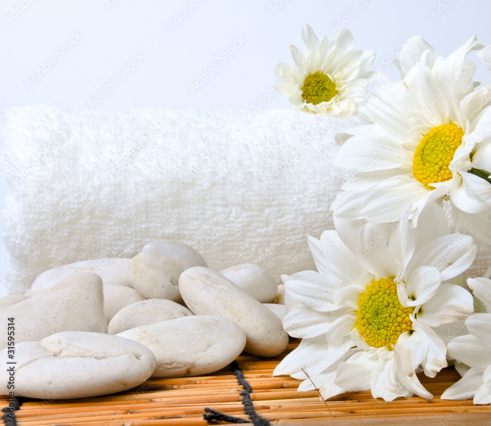The flower , a white towel and stones are on the bamboo mat. All