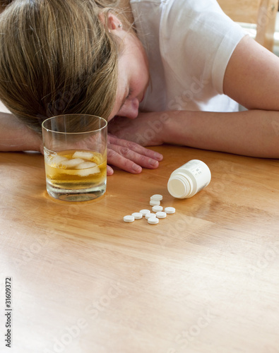Photography close up of pills and alcohol with suicidal woman to background