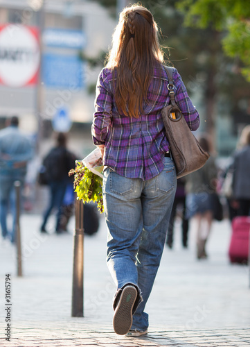 woman wearing jeans walking with a bouquet of flowers in the sun