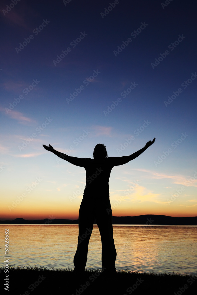 Young woman silhouette raised hands standing at coast