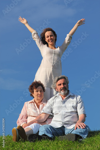 adult daughter with apart hands, parents sitting on grass