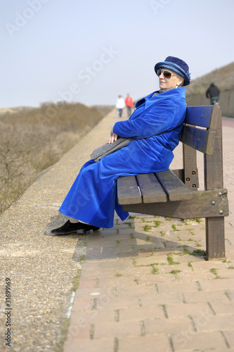 senior woman in blue sitting on a bench at the beach © aldegonde le compte