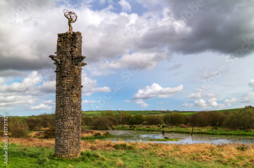 Stone tower with metal tree symbol over Irish landscape