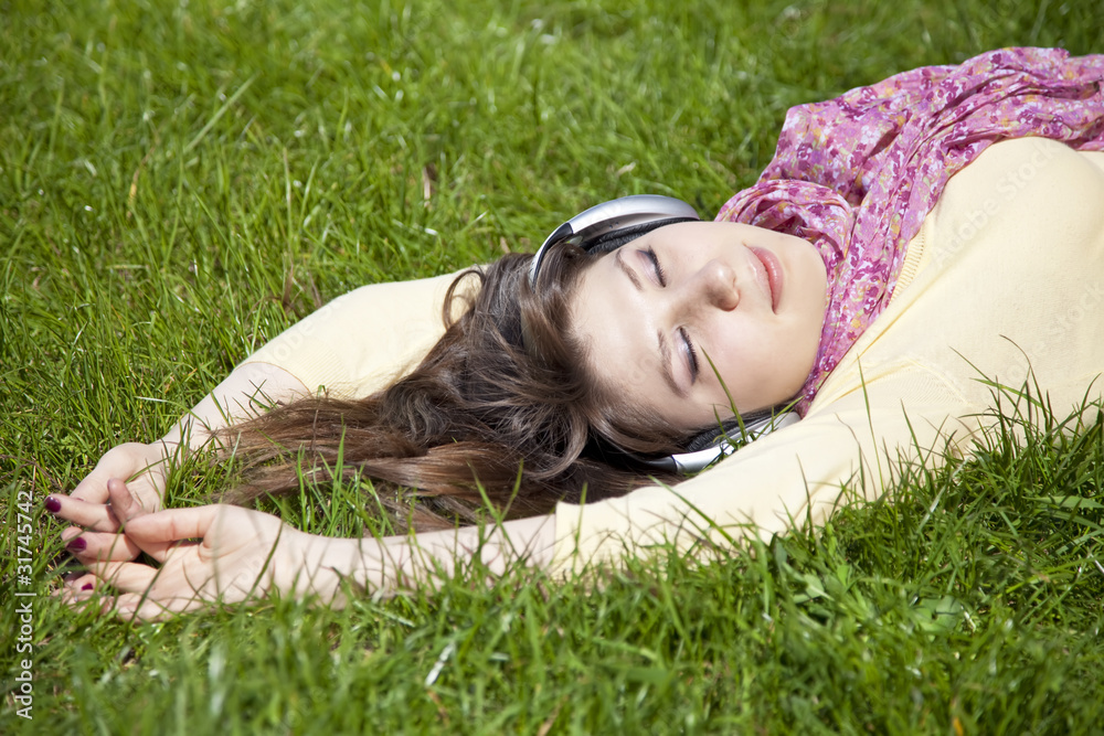 Brunette girl with headphone lies in the park. Brunette girl with headphone lies in the park.