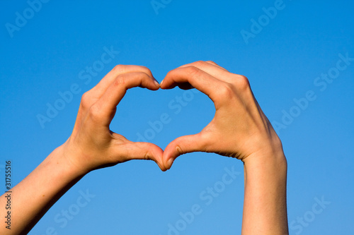 Hands forming heart against blue sky