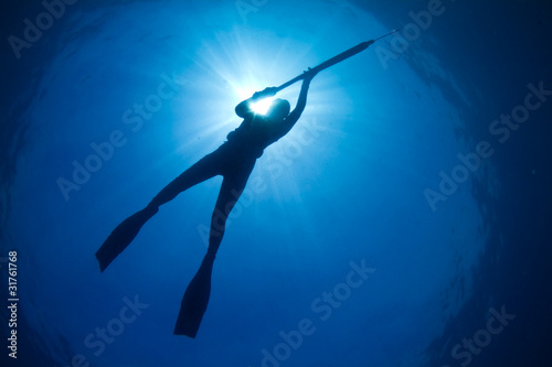 A silhouette of a young woman spearfishing
