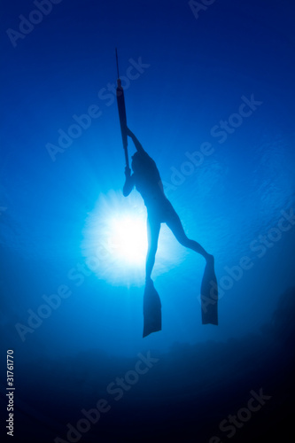A girl spearfishing infront of the sun photo