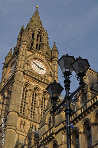 The clock tower of Iconic Manchester town hall with a distinctive old style lamppost against a blue sky 