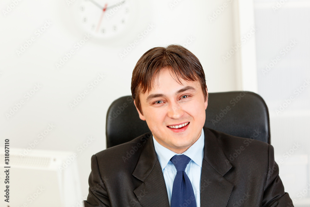 Smiling modern businessman sitting at office desk. Smiling modern businessman sitting at office desk.