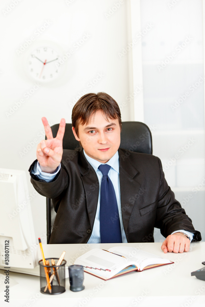 Confident modern businessman in office showing victory gesture. Confident modern businessman in office showing victory gesture.