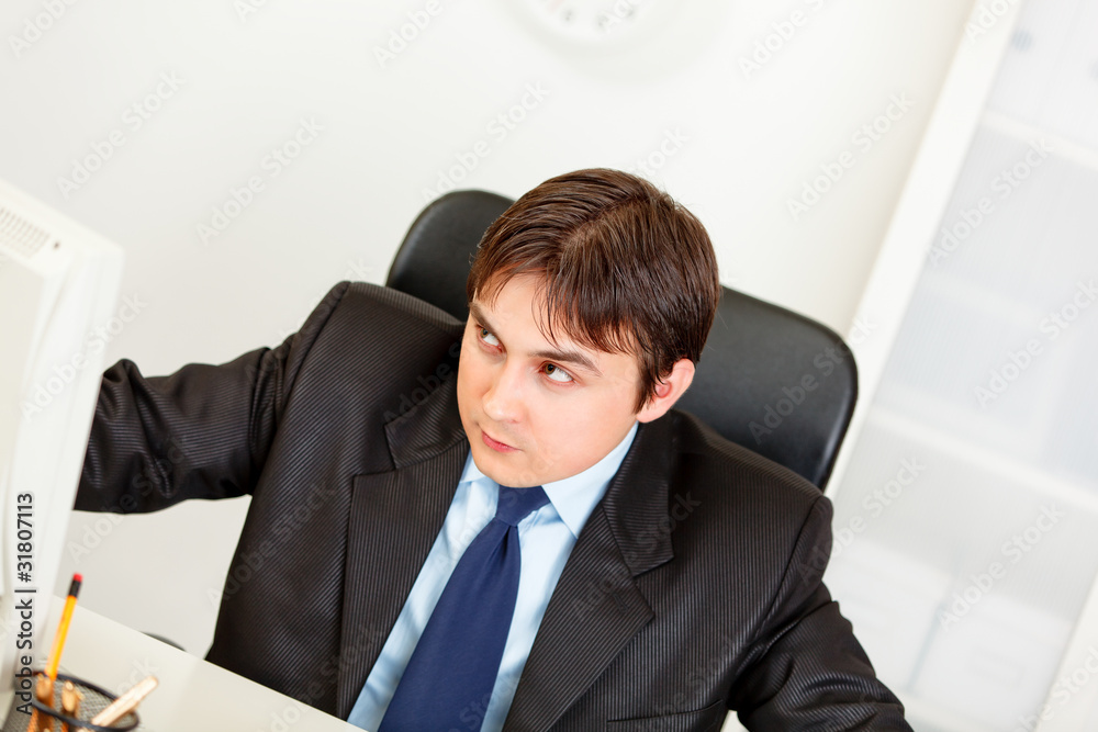 Alert businessman sitting at office desk and looking in corner.