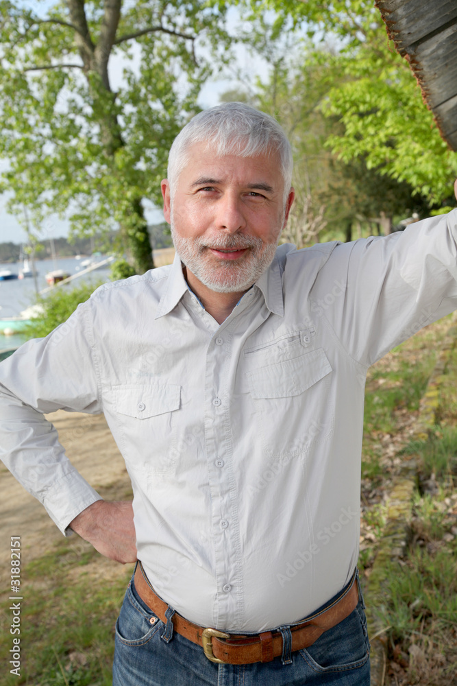 Smiling senior man standing on lakeside Smiling senior man standing on lakeside