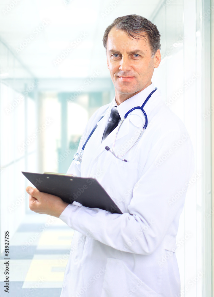 Happy smiling mature doctor writing on clipboard in a Happy smiling mature doctor writing on clipboard in a