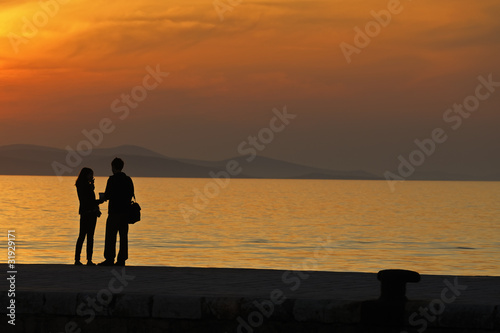 Young couple standing on a jetty at sunset