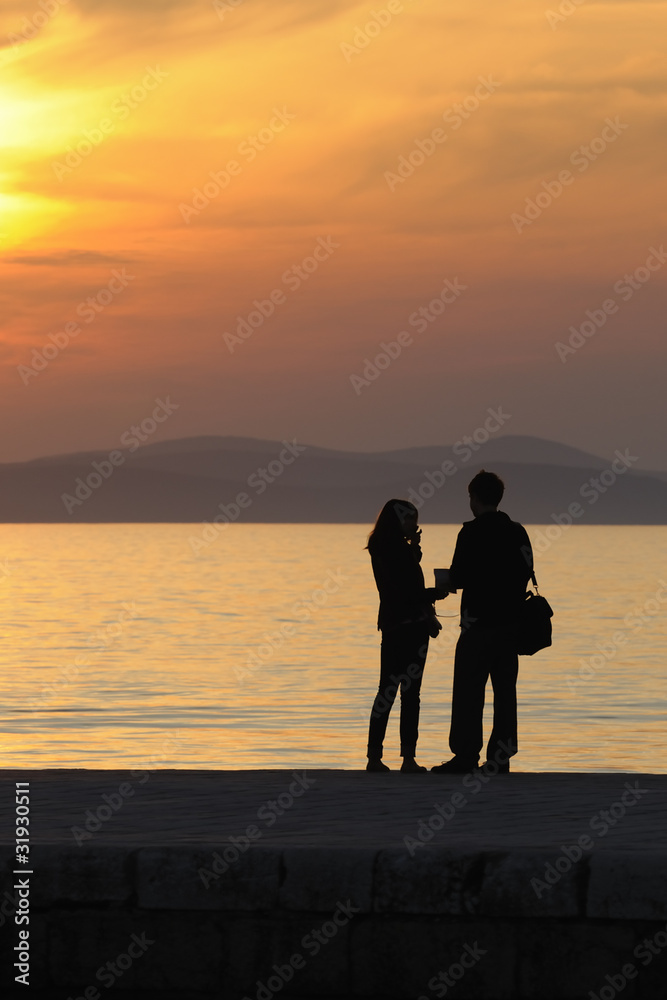 Young couple standing on a jetty at sunset