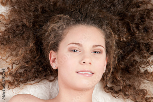 Girl with perfect curly hair lying on fur bed