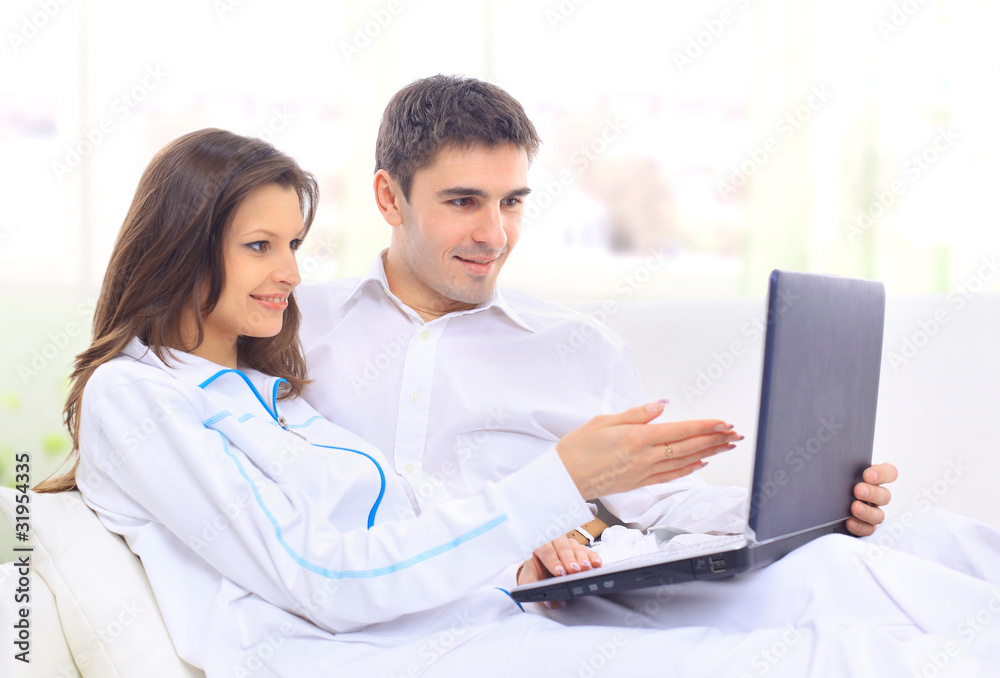 Portrait of a happy young couple sitting on a sofa using Portrait of a happy young couple sitting on a sofa using