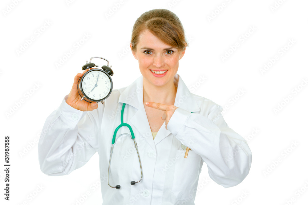 Smiling medical female doctor pointing finger on alarm clock Smiling medical female doctor pointing finger on alarm clock