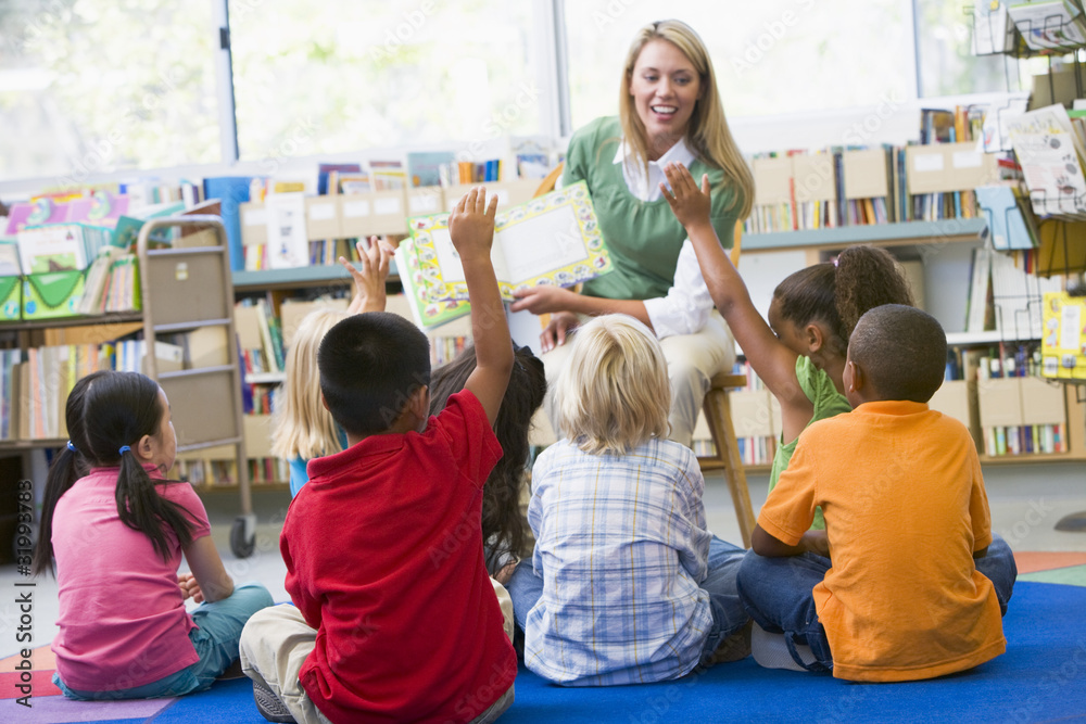 Kindergarten teacher reading to children in library - obrazy, fototapety, plakaty 