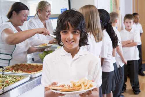 Schoolboy holding plate of lunch in school cafeteria