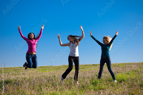 three young beautiful woman jumping into the field against the s