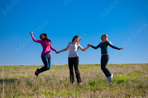 three young beautiful woman jumping into the field against the s