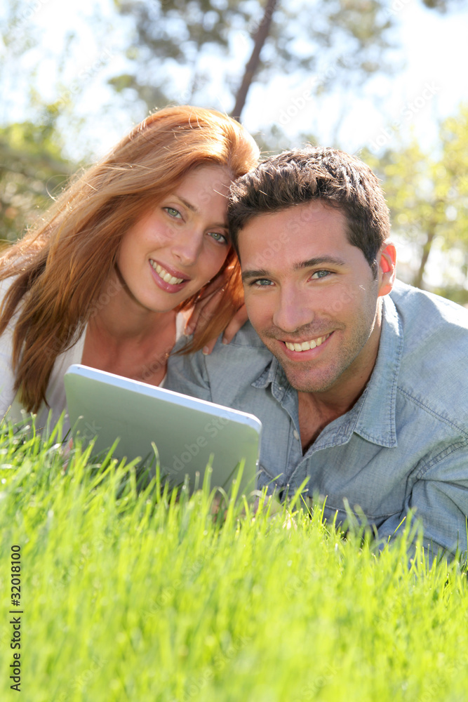 Portrat of couple laying down the grass with touchpad Portrat of couple laying down the grass with touchpad