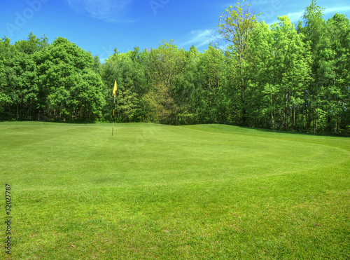 Vibrant image of golf course with flag and fairway in sun