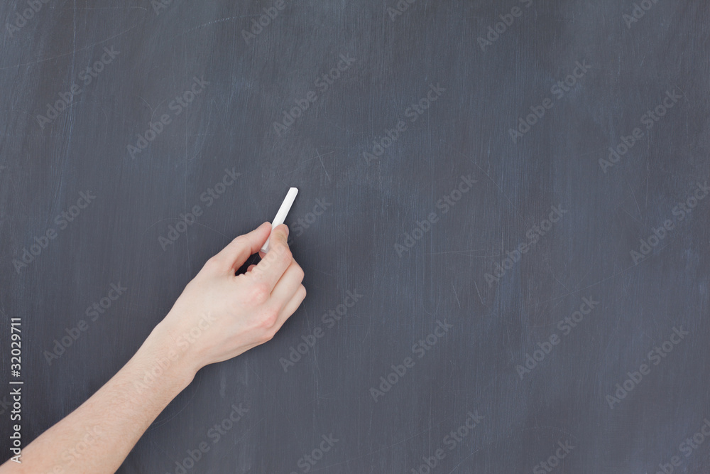Naklejka premium Hand holding a chalk and and ready to write on a blackboard