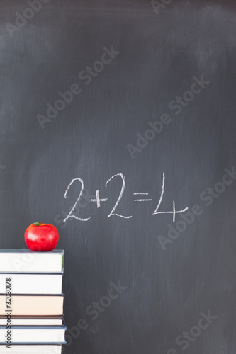 Stack of books with a red apple and a  blackboard with "2+2=4" w