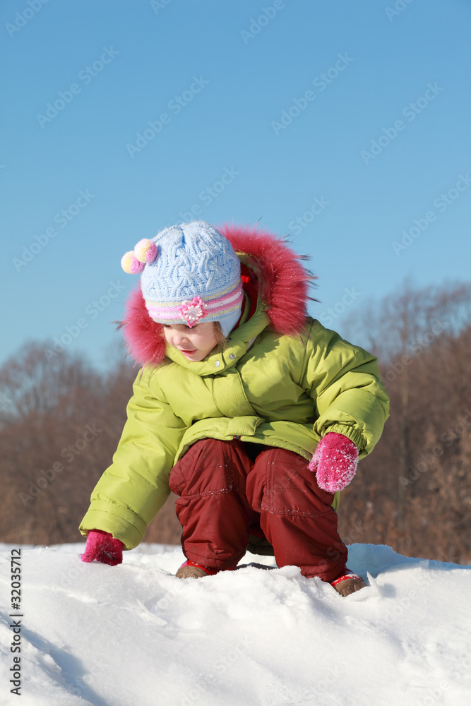 little girl in green jacket sitting at snow outdoors at winter