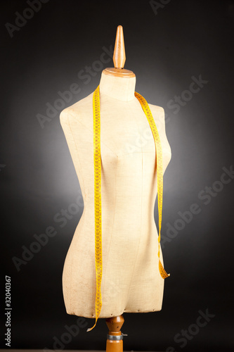 tailor mannequin with tape measure on black background