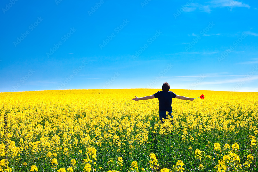 man with pinwheel standing in a field of yellow rape against the