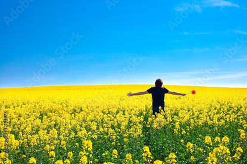 man with pinwheel standing in a field of yellow rape against the
