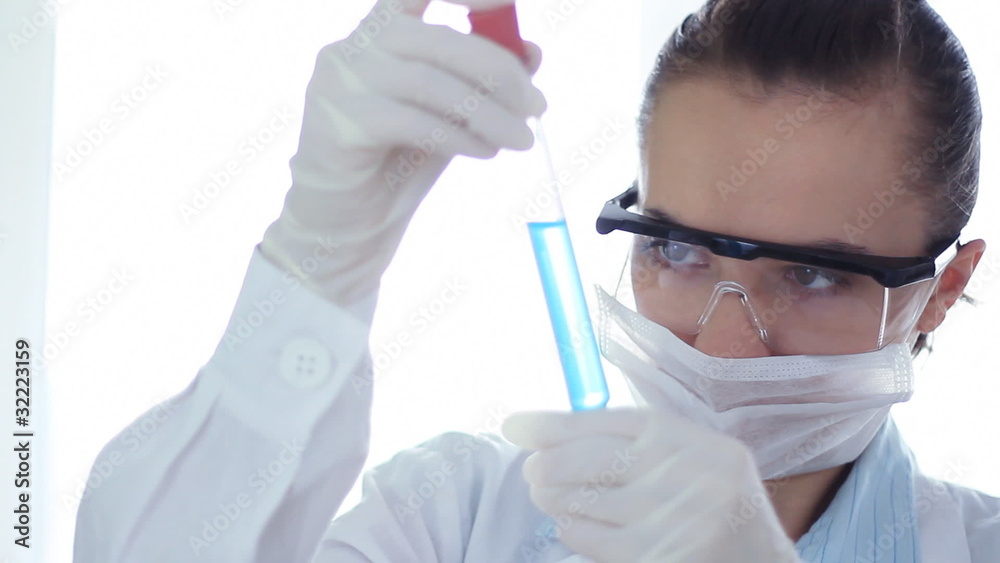 Female scientist looking at test tube with blue liquid Female scientist looking at test tube with blue liquid