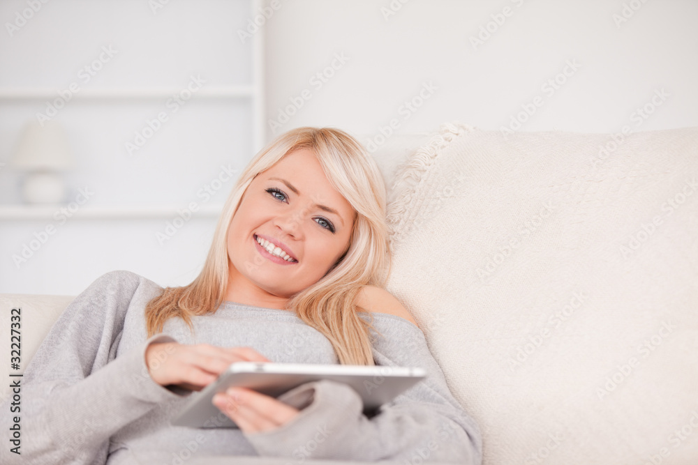 Pretty blond woman lying on a sofa relaxing on a line of tablet Pretty blond woman lying on a sofa relaxing on a line of tablet