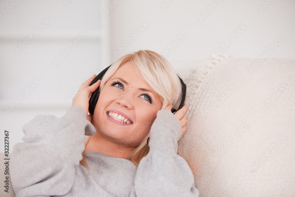 Charming young blond woman with headphones lying in a sofa Charming young blond woman with headphones lying in a sofa