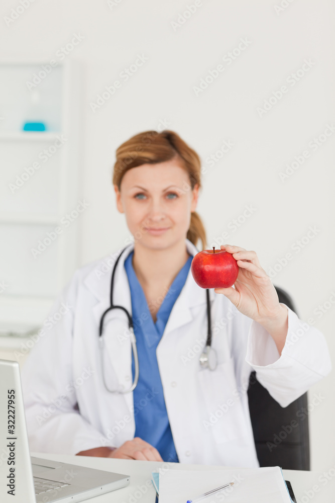 Cute female doctor showing a red apple to the camera in her surg Cute female doctor showing a red apple to the camera in her surg