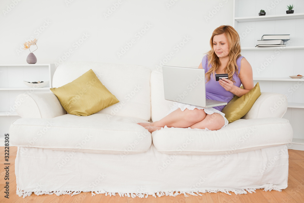 Good looking woman sitting on a sofa is going to make a payment