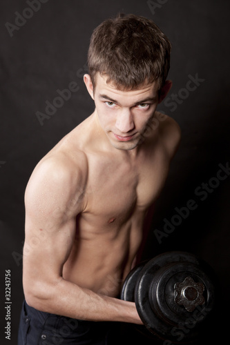 energetic naked man lifting dumbbell against black background